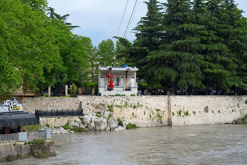 A riverbank cable car station surrounded by lush trees and adjacent buildings, cable car cabin, Rioni River, Kutaisi, Imereti region, Georgia