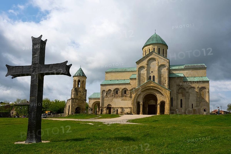 Historic church with cross in the foreground, cloudy sky surrounded by green landscape, Bagrati Cathedral, Church of the Dormition of the Most Holy Mother of God, UNESCO World Heritage Site, Kutaisi, Imereti Region, Georgia