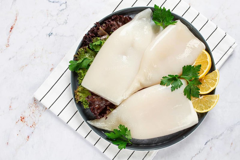 Fresh squid on a black plate with greens and lemon slices prepared for cooking in a kitchen setting