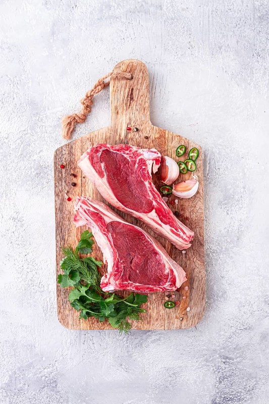 Fresh pieces of beef on the bone, on a wooden cutting board, with herbs and spices, ready for cooking in the kitchen