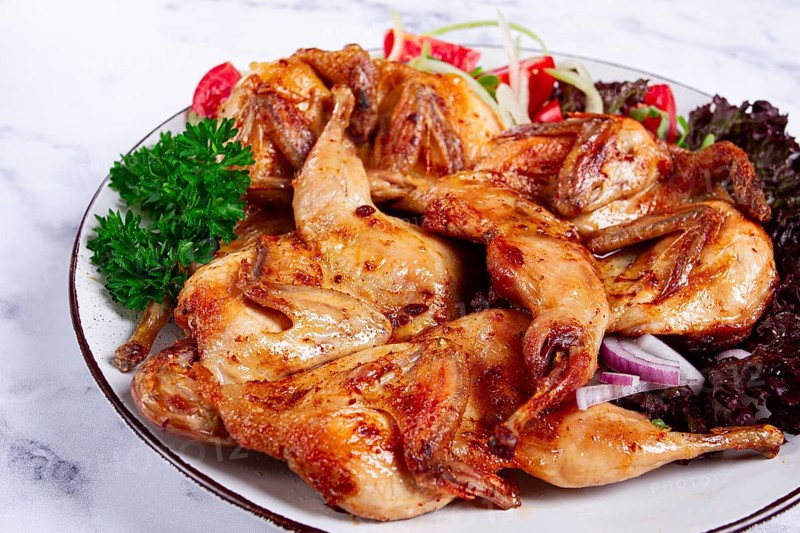 Baked quail, served on a plate with crispy lettuce leaves, fresh tomatoes and herbs, on a white plate, homemade