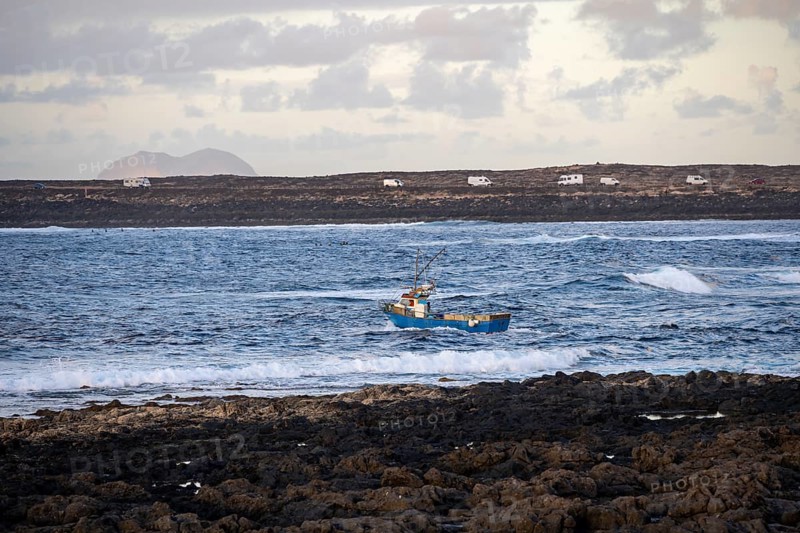 Fishing boat out to sea in the evening, seaside coast with volcanic rocks at sunset, La Santa, Lanzarote, Canary Islands, Spain
