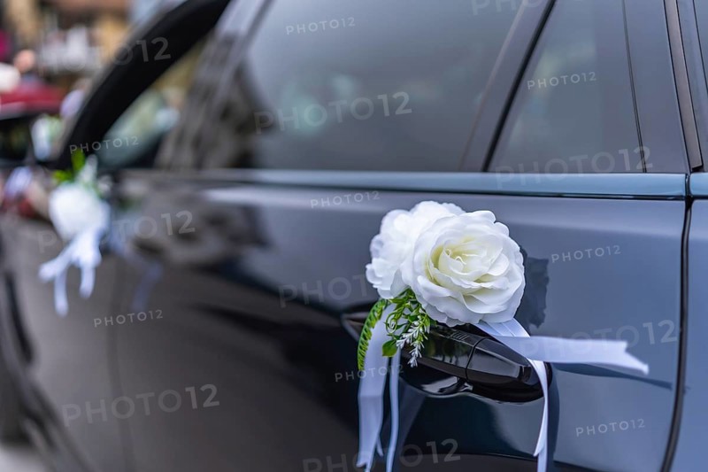 White roses and ribbons elegantly adorn a wedding car door handle, adding a touch of romance and celebration to the special occasion
