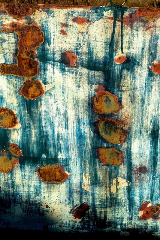 Textured surface revealing rust patterns on a weathered metal sheet in an outdoor setting during daylight