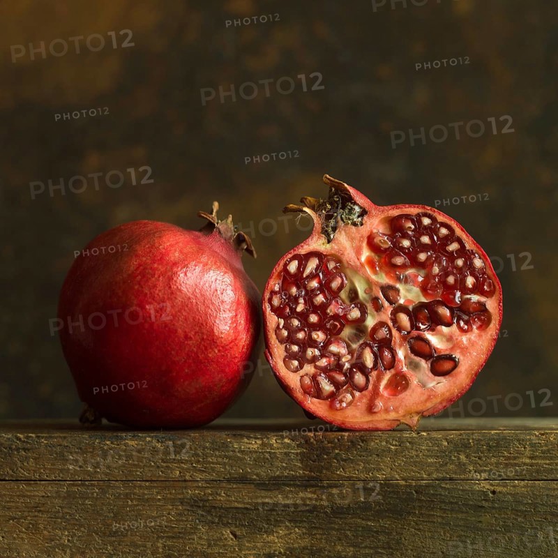 Pomegranate halves revealing juicy seeds on rustic wooden surface