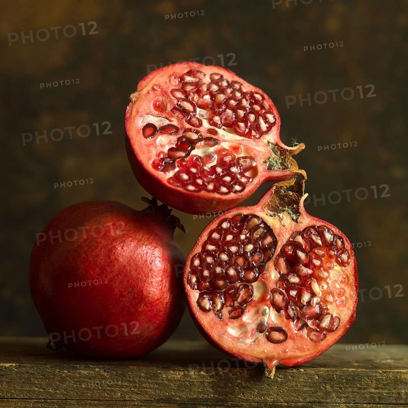 Pomegranates cut in half with seeds exposed on wooden surface in soft lighting