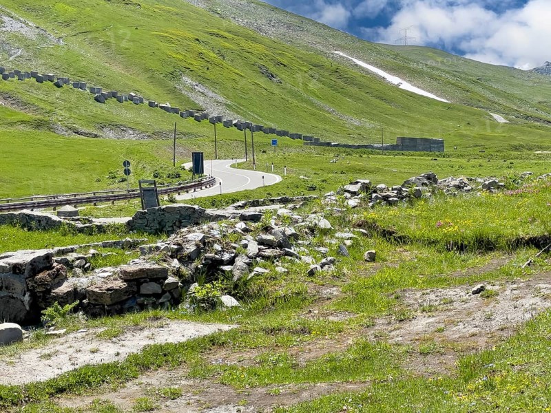 View of the front foundation walls ruins of 2000 year old historical ancient Roman hostel Mansio at the top of the Alpine pass Colle del Piccolo San Bernardo, Col du Petit Saint Bernard Little Saint Bernard Pass in the Alps, behind it modern pass road, in the background on the left on the slope remains of former border fortifications from World War II, Aosta Valley region, Italy