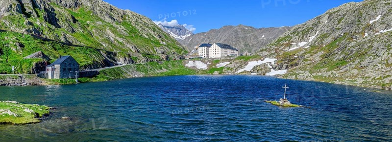 Panoramic photo of mountain lake Alpine lake Lac du Grand Gd Saint St Bernard, on the left Swiss border station border building for passport control, on the right in front Christian cross on small rocks in the lake near the shore centre in the background building with hostel Auberge and Hospice Hospice on Alpine pass Great Saint Bernard Col du Grand Gd Saint St Bernard Colle del Gran San Bernardo, Aosta Valley region, Italy, Canton Valais, Switzerland