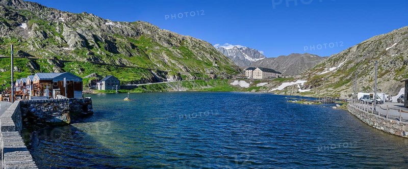 Panoramic photo of mountain lake Alpine lake Lac du Grand Gd Saint St Bernard, on the left souvenir shops, behind it Swiss border station border building for passport control in the background building with hostel Auberge and hospice Hospice on Alpine pass Great St Bernard Col du Grand Gd Saint St Bernard Colle del Gran San Bernardo, region Valle d'Aosta, Italy, canton Valais, Switzerland