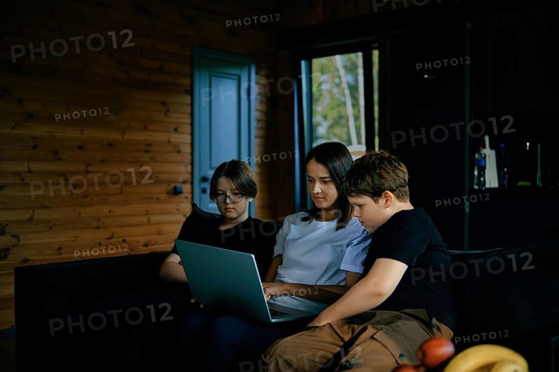 The family enjoys spending time together watching a movie on a laptop in a cozy wooden cabin