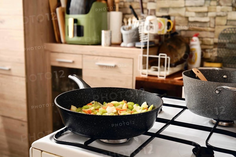 Fresh vegetables in a frying pan on the stove, showcasing a vibrant mix of colors. A cozy kitchen with wooden cabinets and modern appliances enhances the cooking experience