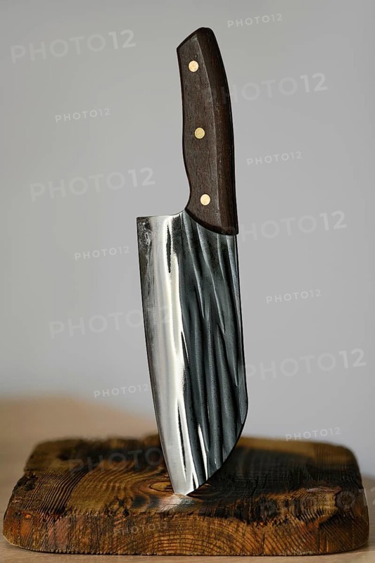 Serbian kitchen knife stuck in a rustic wooden block. The knife features a sleek, shiny blade with unique patterns and a dark wooden handle. Ideal for culinary enthusiasts