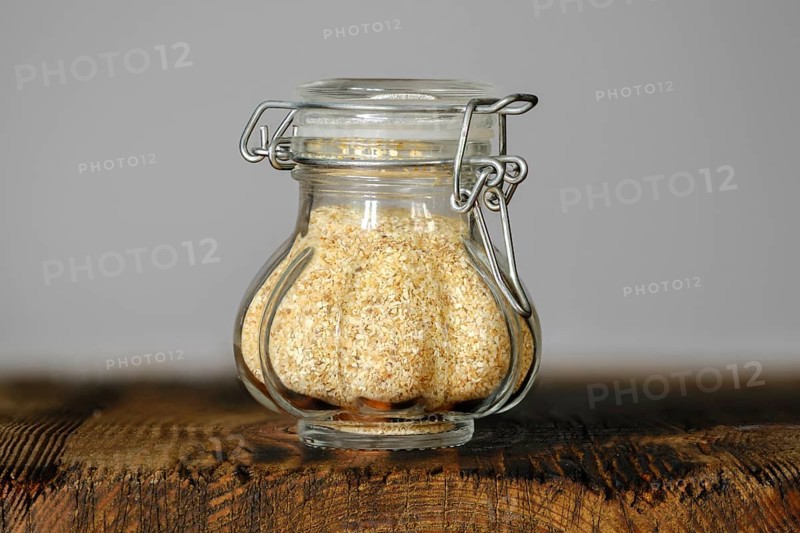 A small, decorative glass jar with garlic flakes, showcasing its fine texture and color on a rustic wooden surface