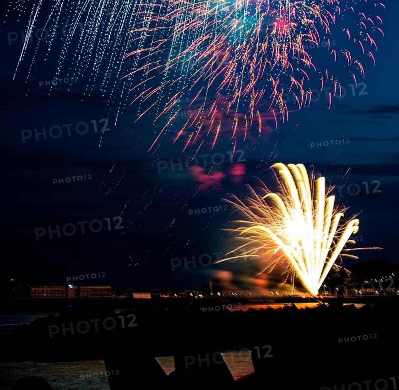Brightly shining atmospheric fireworks for the Helgoland island festival in red, blue and gold over the nocturnal lowlands, inland port, jetty and lobster shacks, in front the stages of the dune made of tetrapods and the reflecting water of the North Sea, night sky at the island festival in summer, symbolic image also for New Year's Eve, New Year's Eve fireworks, bright, colourful, many colourful traces of light, sparks, lively glitter, night, island of Helgoland, Schleswig-Holstein, Germany