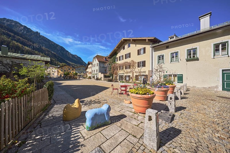 Old town, historic houses, square, cobblestones, bollards, wooden fence, facade, windows, bushes, flower pots, Easter decoration, mountain landscape, mountains, forest, blue sky, cirrostratus clouds, Florianiplatz, Bad Reichenhall, district Berchtesgadener Land, Bavaria, Germany