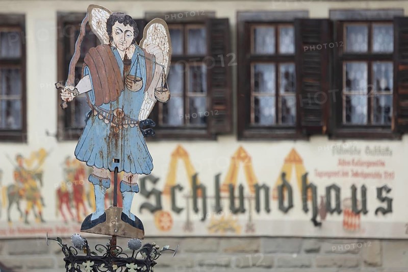 Figure at the Luitpold fountain built in 1911, fountain, angel, sword, stabbing weapon, beam balance, symbol, Justitia, sheet metal, metal, hotel, Schlundhaus, inscription, depth of field, blur, market square, Bad Königshofen, Rhön, Lower Franconia, Franconia, Bavaria, Germany