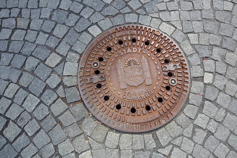 Round manhole cover with town coat of arms, inscription, cobblestones, floor, Ilmenau, Thuringian Forest, Thuringia, Germany