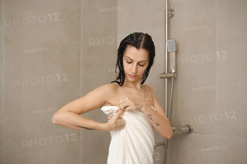 In a modern bathroom, a woman with damp hair adjusts her towel after taking a shower. She appears relaxed as she prepares for her morning routine in a bright and inviting space