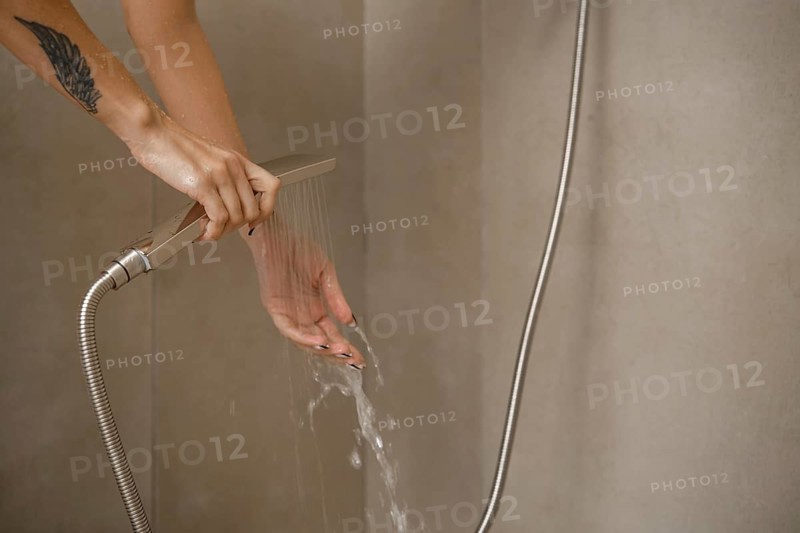Hands are positioned under flowing water from a sleek showerhead in a stylish bathroom. The setting features clean lines and neutral walls, emphasizing a relaxing ambiance during personal care