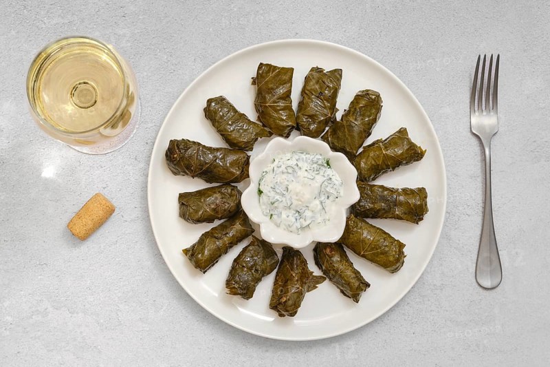 Dolma is being prepared at home, featuring grape leaves stuffed with rice, lamb meat and herbs, served with tangy yogurt sauce