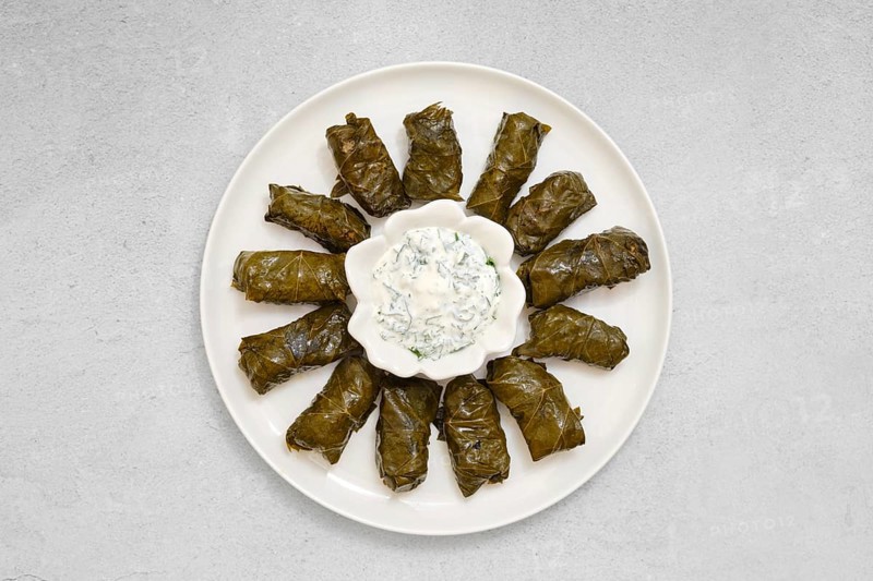 Freshly prepared dolma sits on a plate, featuring stuffed vine leaves neatly arranged. A bowl of creamy yogurt dip lies in the center, perfect for enhancing the dish's flavors