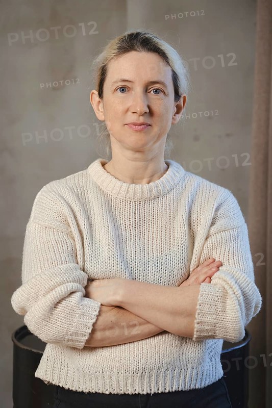 A woman poses confidently with her arms crossed, dressed in a soft, knitted sweater