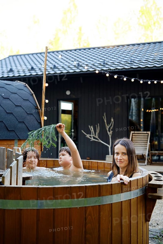 Two children and their mother playfully enjoy an outdoor hot tub at a charming cabin