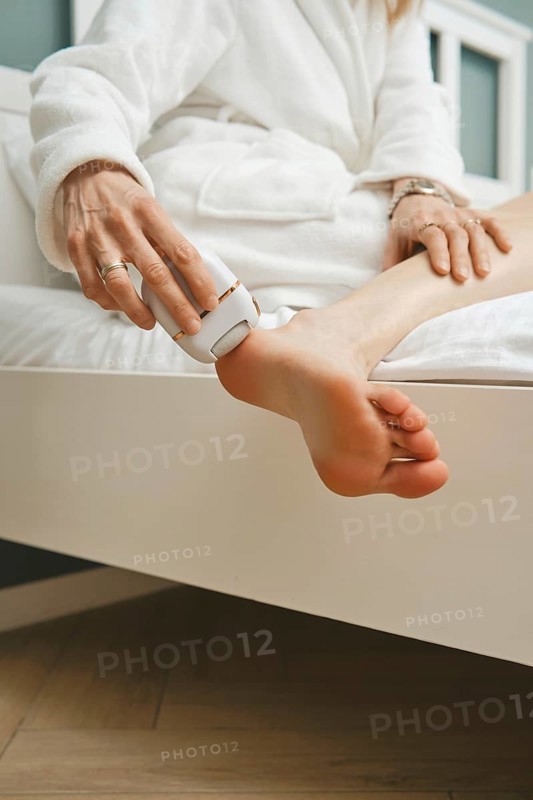 Close-up view of peeling dead skin off heel with handheld electric exfoliating machine in bedroom