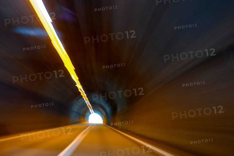 View from car while driving fast on car driver speeding car racer through long tunnel with straight tunnel tube with light at the end of long of a long tunnel above narrow light strips ceiling lighting, international