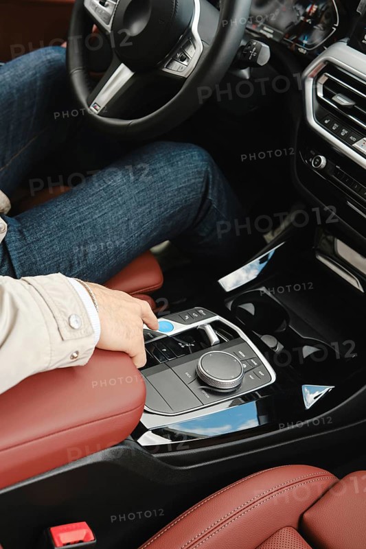 A person in casual attire sits in the driver's seat of a modern vehicle, reaching to adjust the controls located on the center console