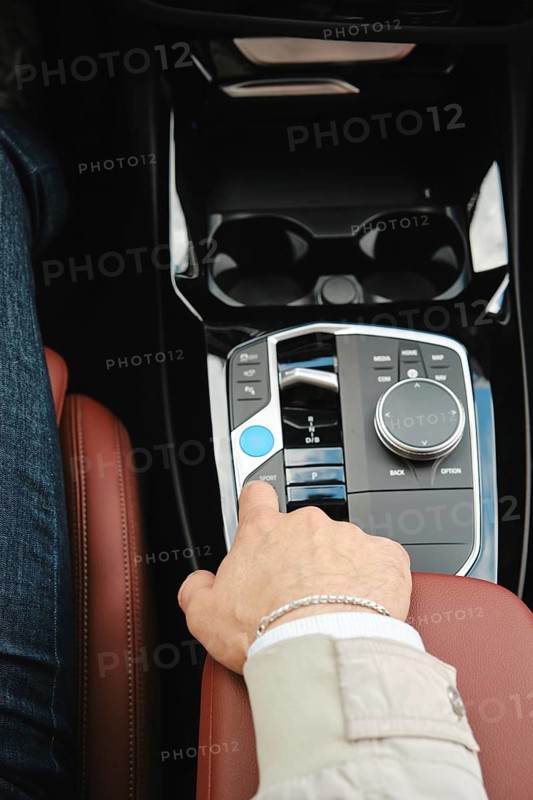 A driver is adjusting the controls in a luxury vehicle. The focus is on the comfortable leather seat and the sleek, modern dashboard design