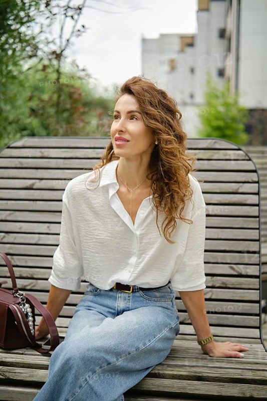 Woman sitting on a bench in a park, enjoying her surroundings during a sunny afternoon