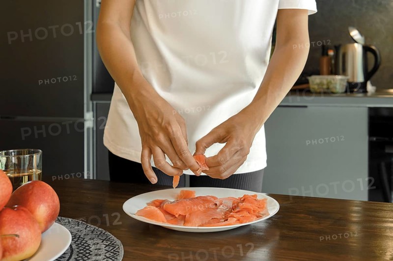 A person is arranging fresh salmon slices on a white plate in a stylish kitchen showcasing a focus on nutritious food preparation