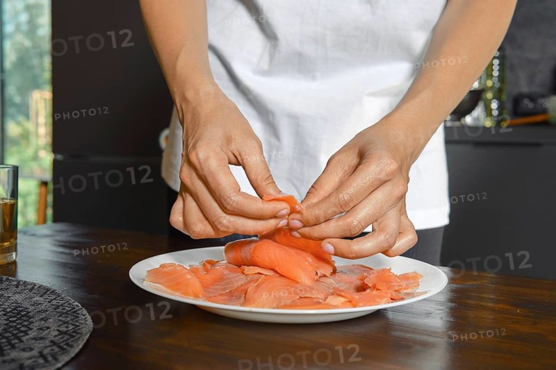 Hands expertly handle smoked salmon fillets on a plate, showcasing a focus on healthy food preparation. Natural light streams in, highlighting the vibrant colors of the dish