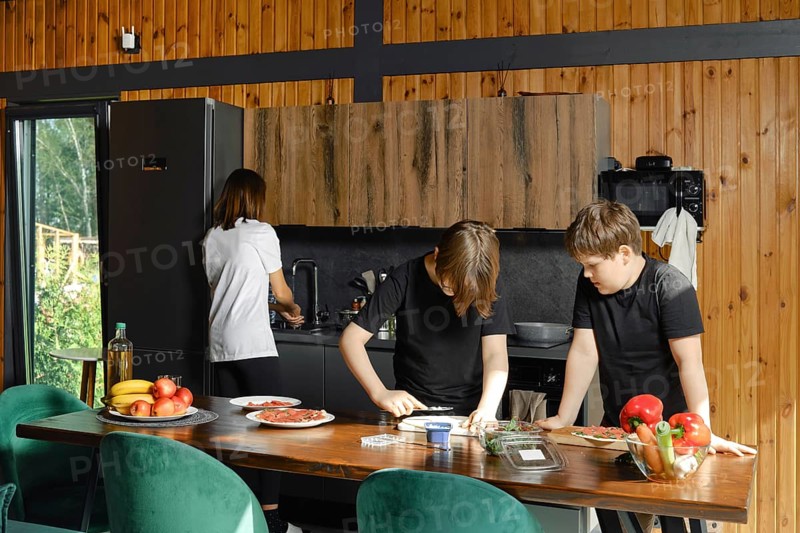 Mother washes dishes while her sons are preparing healthy breakfast in a spacious kitchen of a country house