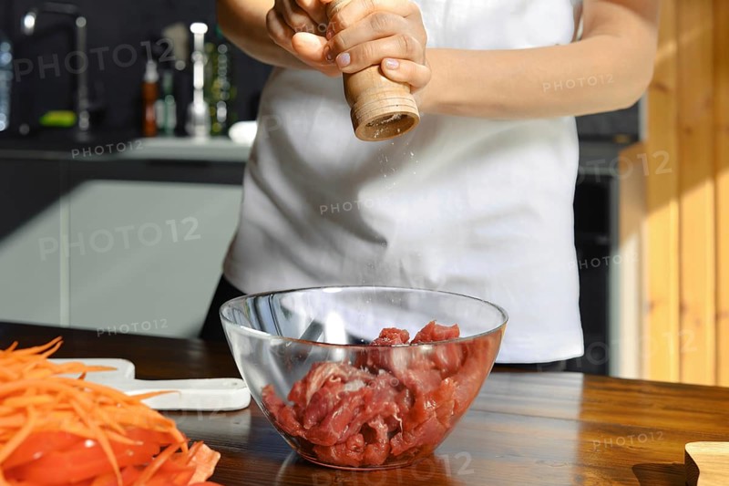 Unrecognizable person is adding freshly ground salt to a bowl of diced meat, preparing for a healthy meal