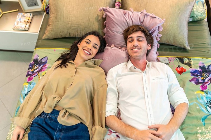 Young couple smiling and lying on a bed, testing comfort together while shopping for home goods in a vibrant home improvement store