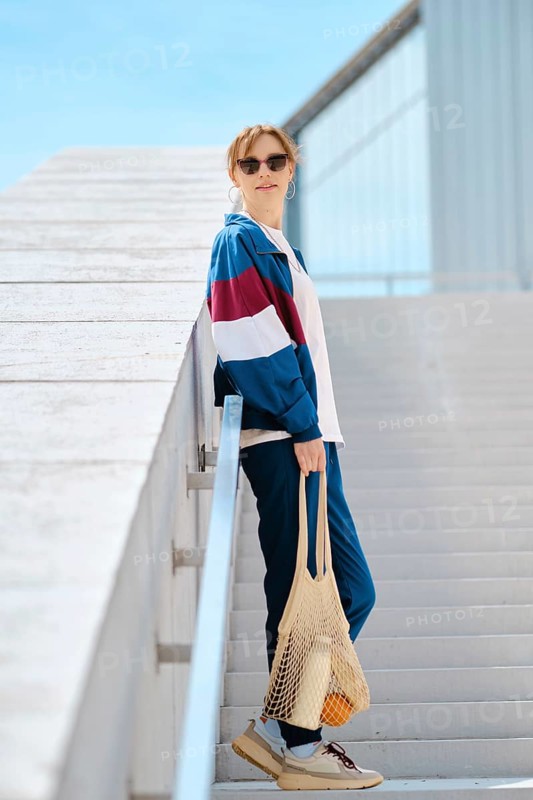 A young sporty woman with string bag stands on a staircase, dressed in stylish athletic track suit