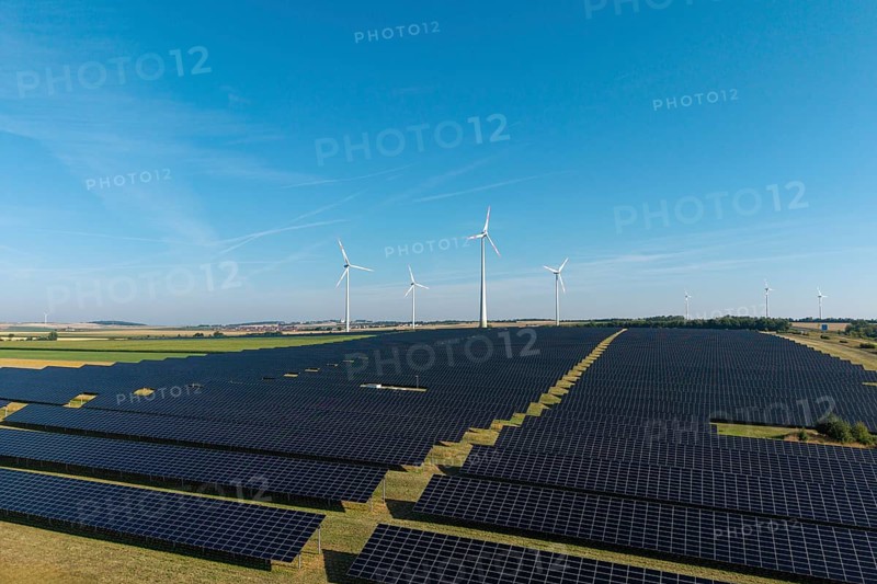 Field full of solar panels with wind turbines in the background under a clear sky, near Kitzingen, Lower Franconia, Bavaria, Germany