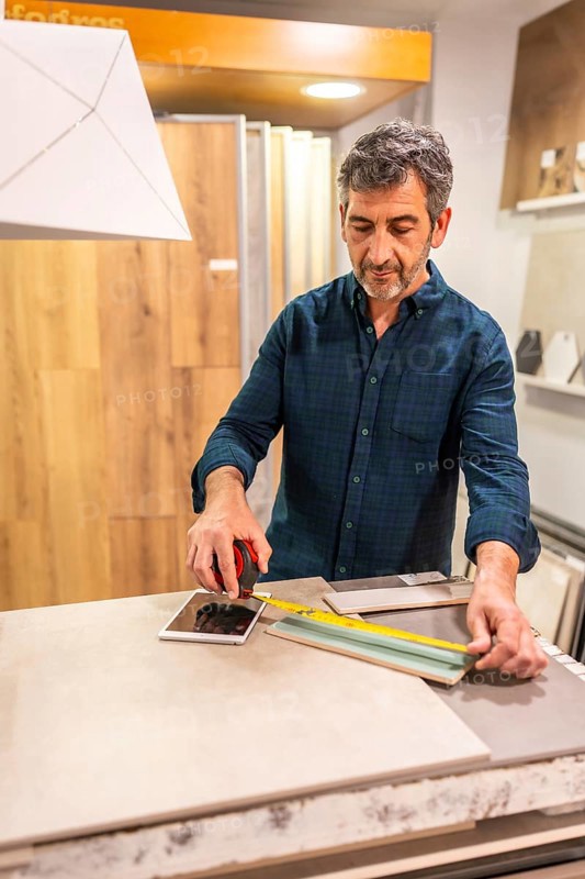 Architect taking measurements of ceramic tile using a tape measure and tablet in a home improvement store showroom
