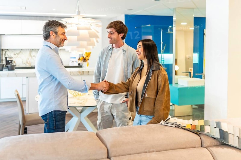 Young couple shaking hands with salesman after choosing new furniture for their apartment in a showroom