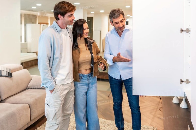 Smiling shop assistant showing a white cabinet door to a young couple, helping them choose furniture for their new home