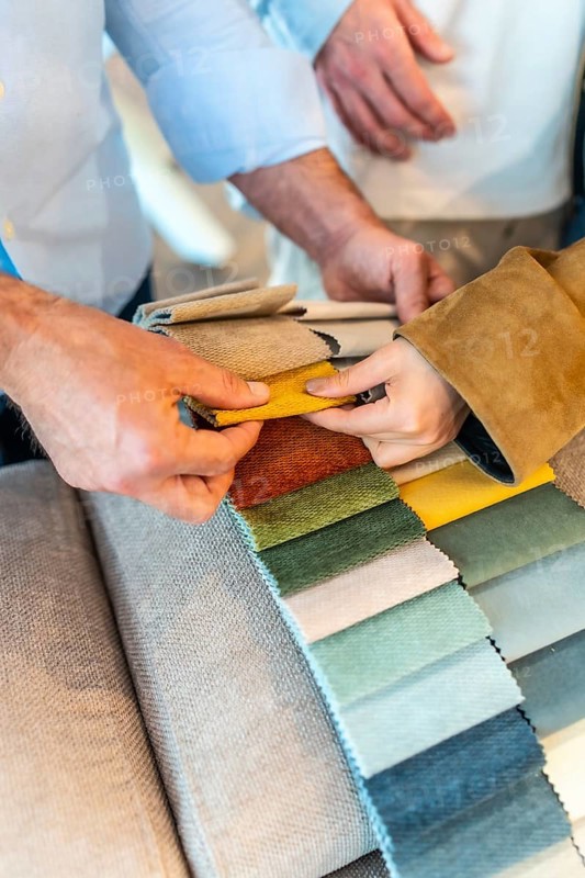 Customers and sales assistant choosing upholstery fabric from a wide variety of colors and textures in a furniture or home improvement store