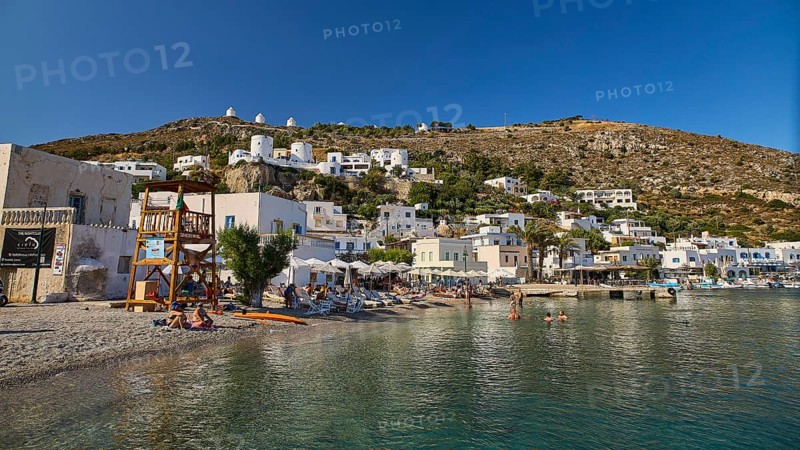 Beach promenade on a clear blue sea, behind it Mediterranean town and windmills on hill, Pandeli Castle, Leros Castle, St John's Fortress, Apitiki Hill, Pandeli Bay, Agia Marina, Leros, Dodecanese, Greek Islands, Greece