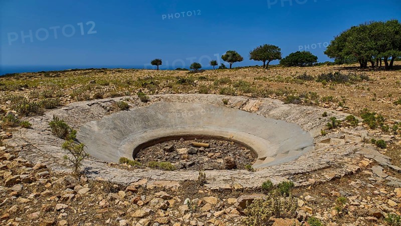 Dry terrain with a crater and scattered trees under a clear sky, Lost Place, Air Defence Position, Aerophone, Parabolic Acoustic Mirror, Patella Mountain, WW2, west of Lakki, Leros, Dodecanese, Greek Islands, Greece