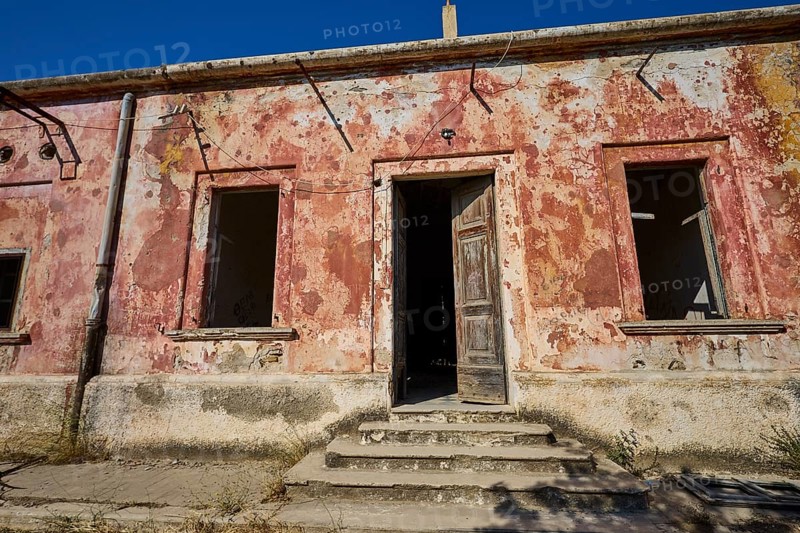 Lost Place, Abandoned house facade with peeling red plaster and open windows under a blue sky, Radio Station, WW2, Agios Nikolaos Radio, Agia Marina, Leros, Dodecanese, Greek Islands, Greece