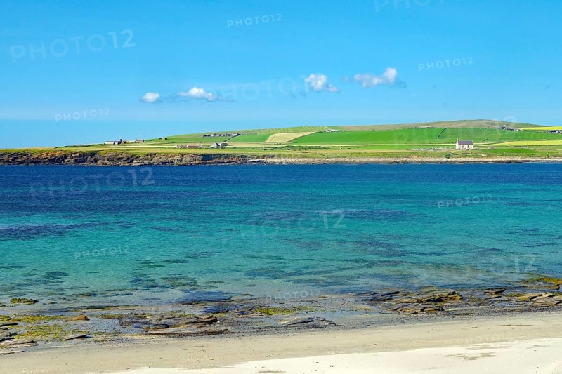 Clear blue sky over a coastal landscape with green shore and crystal clear water, Skara Brae, Neolithic settlement, Mainland, Orkney Islands, Scotland, United Kingdom