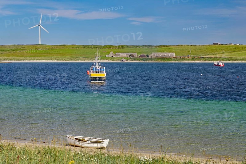 Colourful coastal landscape with boat, windmill and vast water under blue sky, Lambholm, Orkney Islands, Scotland, Great Britain