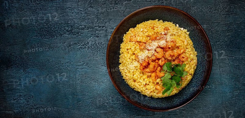 Risotto with shrimp, in a bowl, on a textured surface, with a side dish of fresh coriander, homemade, no people