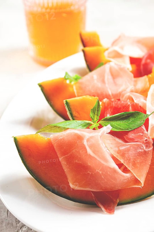 Cantaloupe melon with prosciutto and fresh basil, on a white plate, natural light